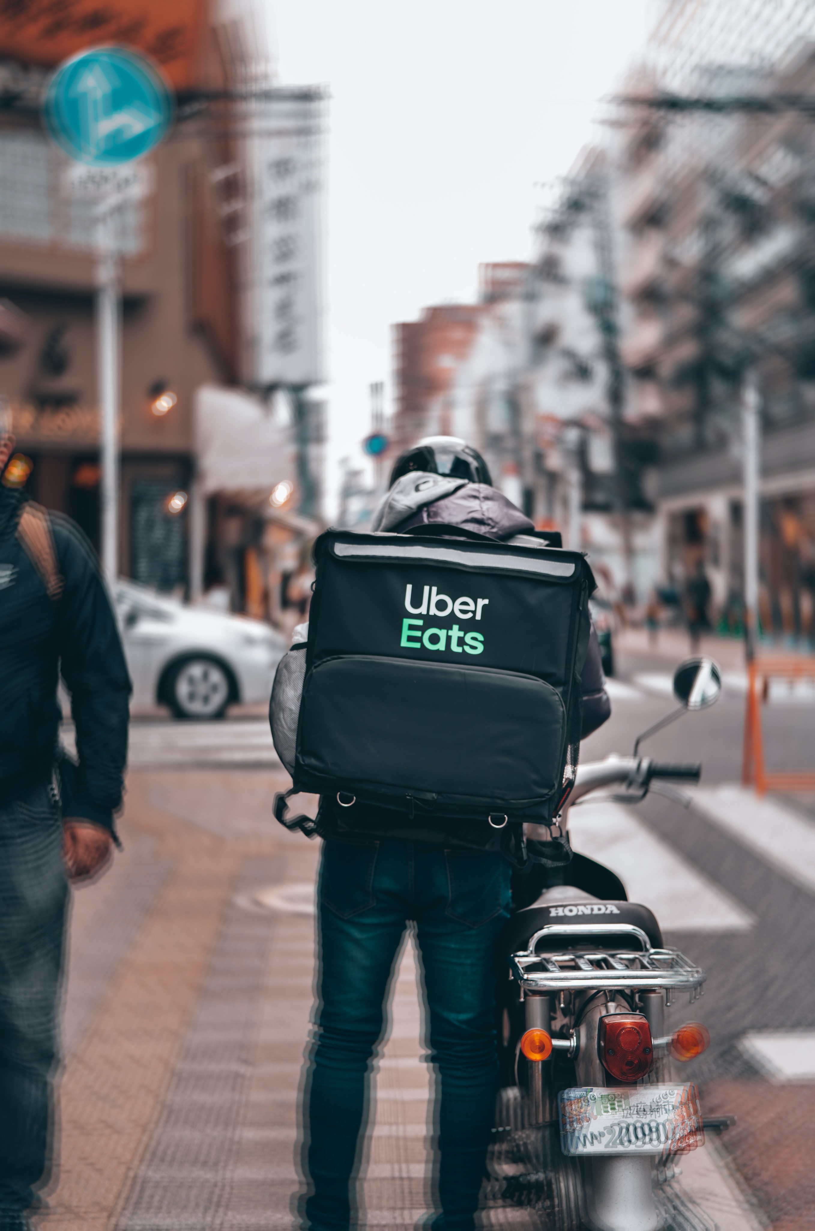 man in black jacket and blue denim jeans with black backpack walking on sidewalk during daytime